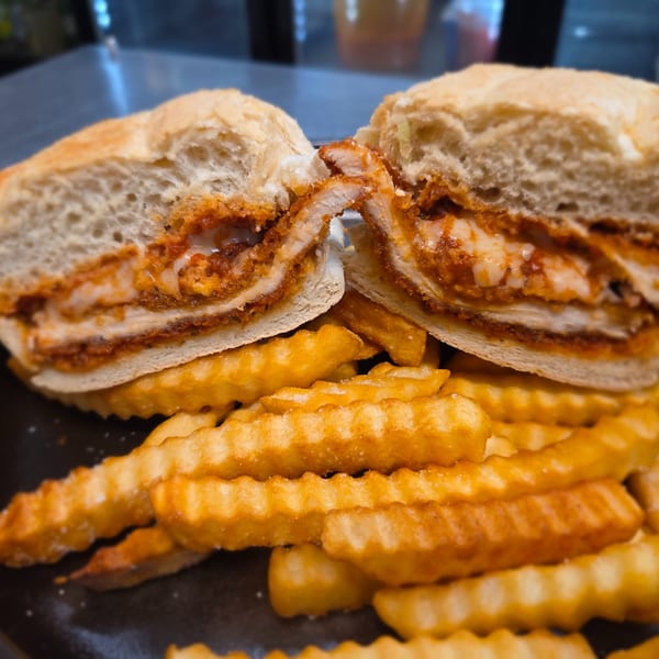 Chicken parmesan sandwich with melted cheese and sauce, cut in half, served with crinkle-cut fries.