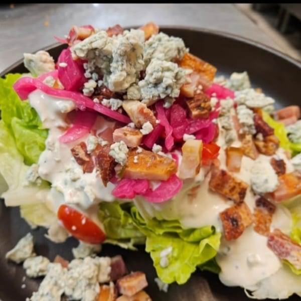 Wedge salad with blue cheese, bacon, pickled onions, and cherry tomatoes on a dark plate.