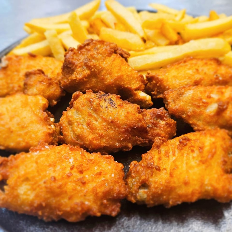 Crispy fried chicken wings and golden french fries on a dark plate.