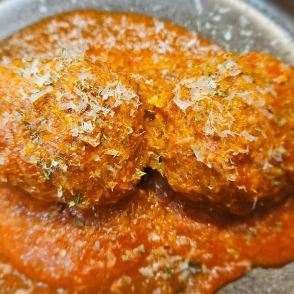 Close-up of two meatballs covered in rich orange sauce, topped with grated cheese and herbs.