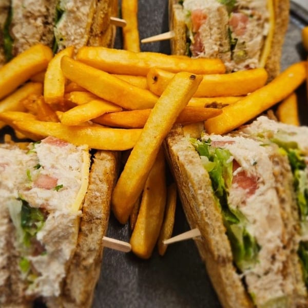 Close-up of a club sandwich with fries, featuring chicken, lettuce, and tomato on toasted bread.