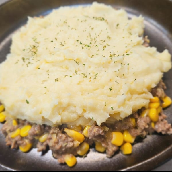 Close-up of a shepherd's pie with mashed potatoes, ground meat, and corn in a dark dish.