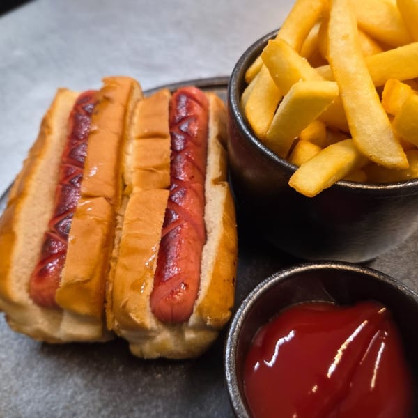 Two grilled hot dogs in buns with a side of golden french fries and a small bowl of ketchup.