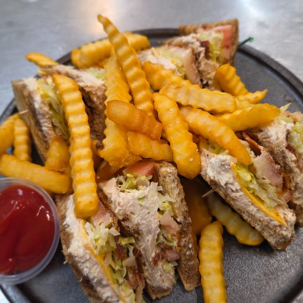 Club sandwiches with crinkle-cut fries and a side of ketchup on a dark plate.