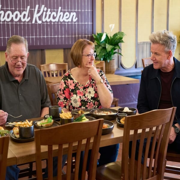 Three people, including Gordon Ramsay, seated at a table with American dishes at The Neighborhood Kitchen.